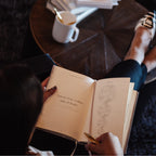 Person reading a book with a quote, sitting on a couch with a cup and books in the background.