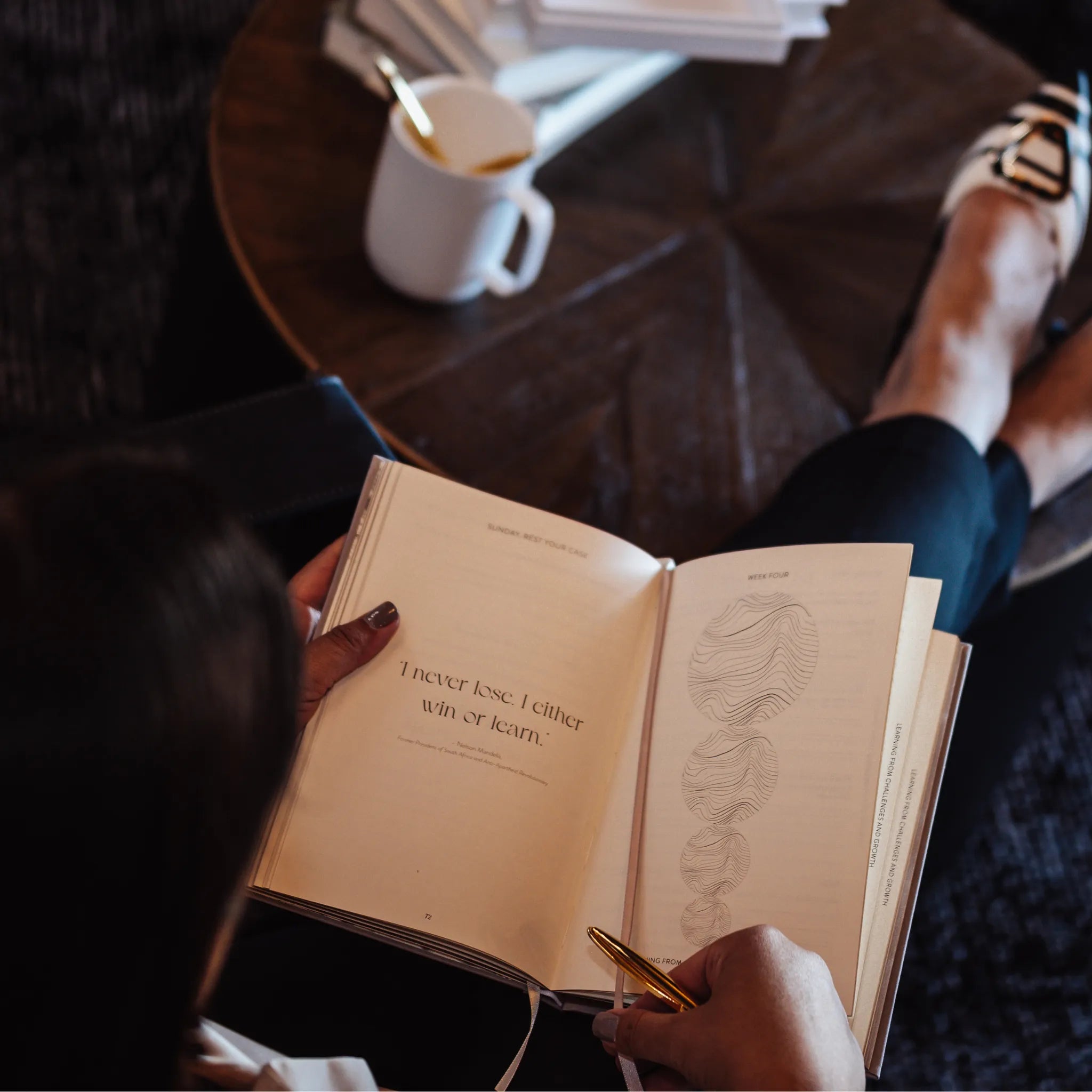 Person reading a book with a quote, sitting on a couch with a cup and books in the background.