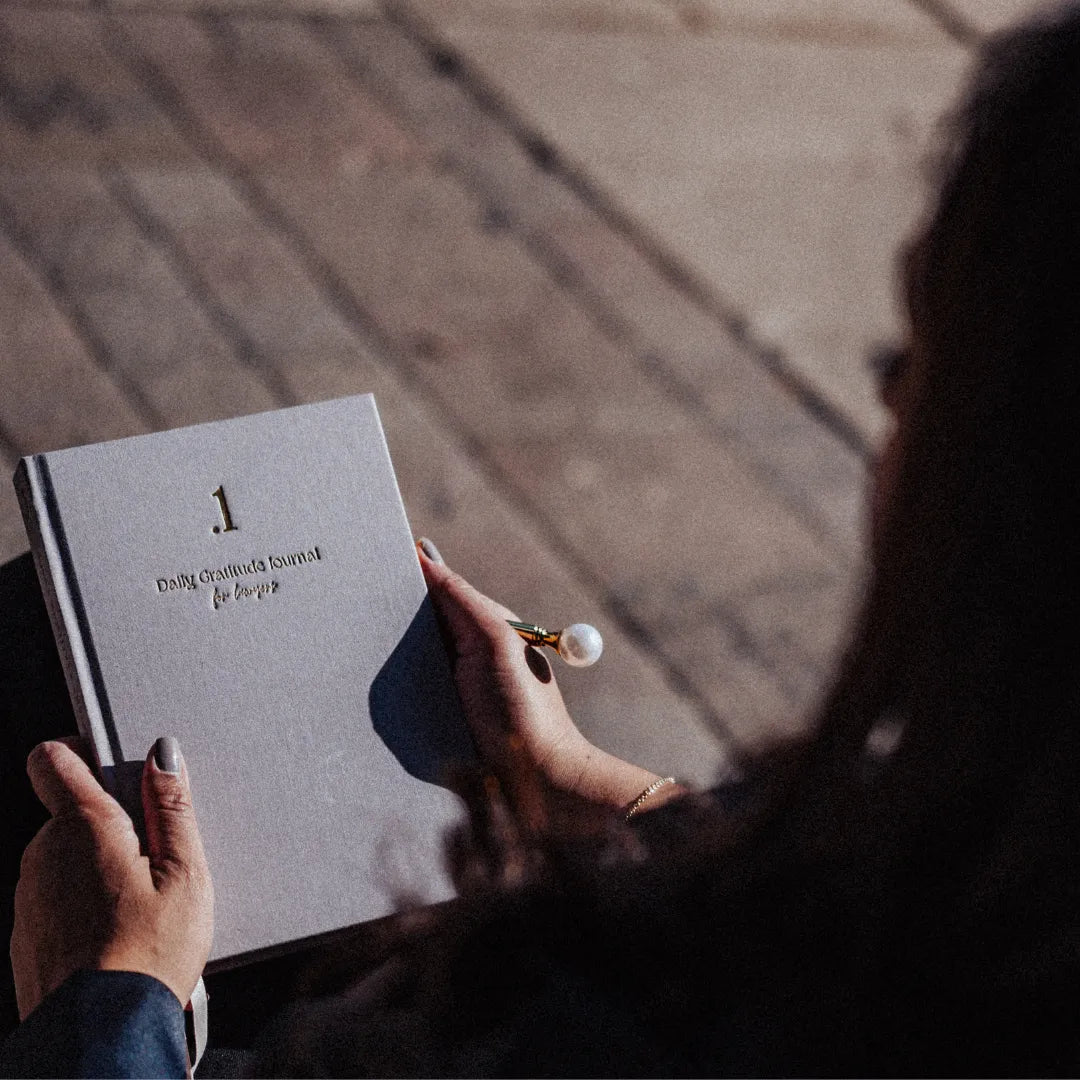 Person holding a book titled '.1 Daily Gratitude Journal for Lawyers' with a pen, blurred background