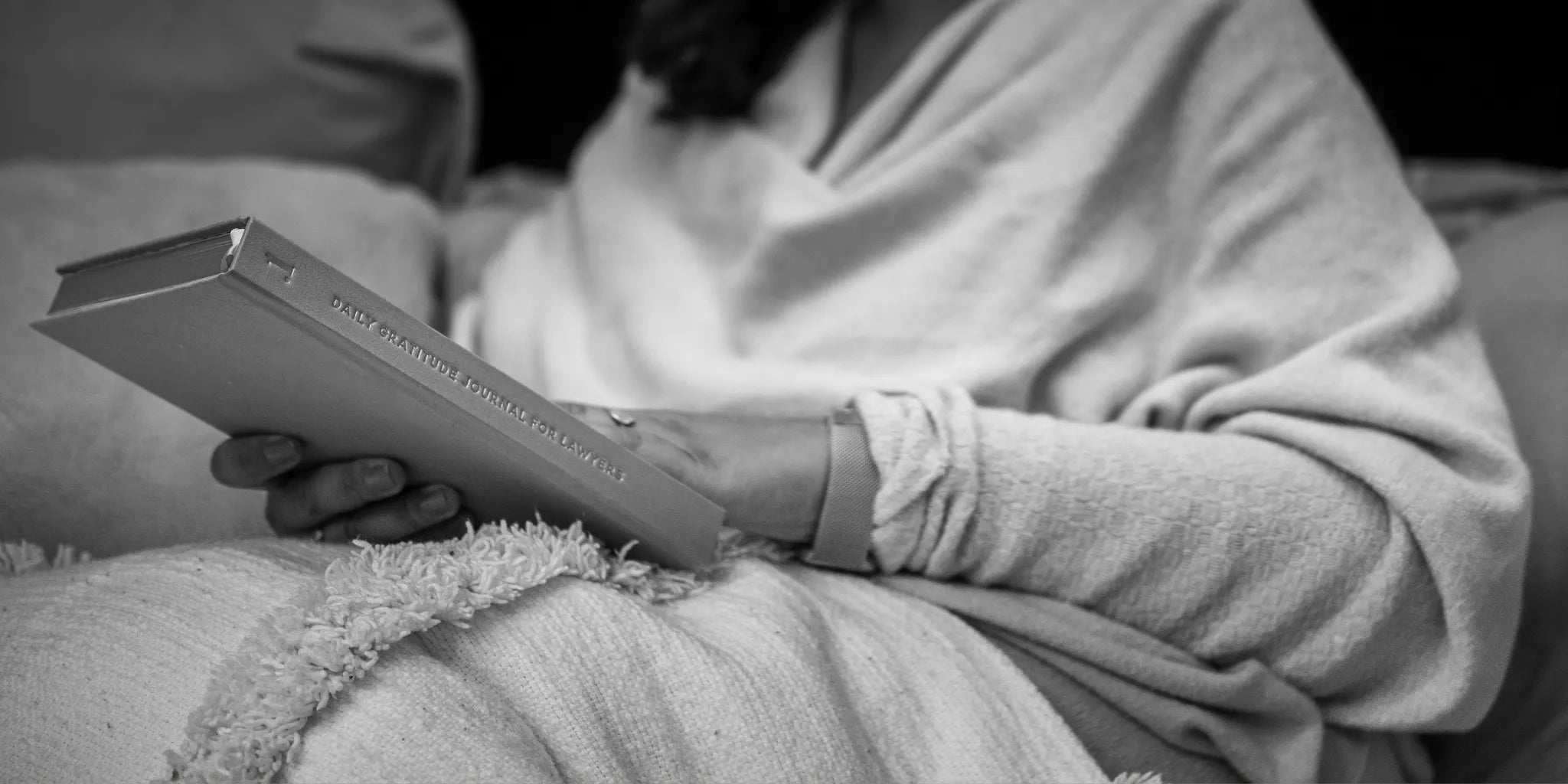 Person holding a book titled '.1 Daily Gratitude Journal for Lawyers' wrapped in a blanket on a couch