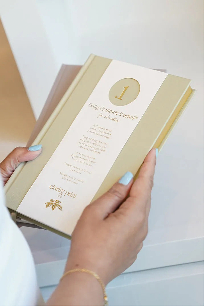 Person holding a calming green daily gratitude journal with gold accents in an indoor setting