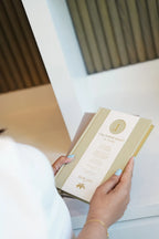 Person holding a beige book with gold accents in an indoor setting