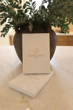 Vase with greenery and a card displaying 'clarity print' on a marble surface
