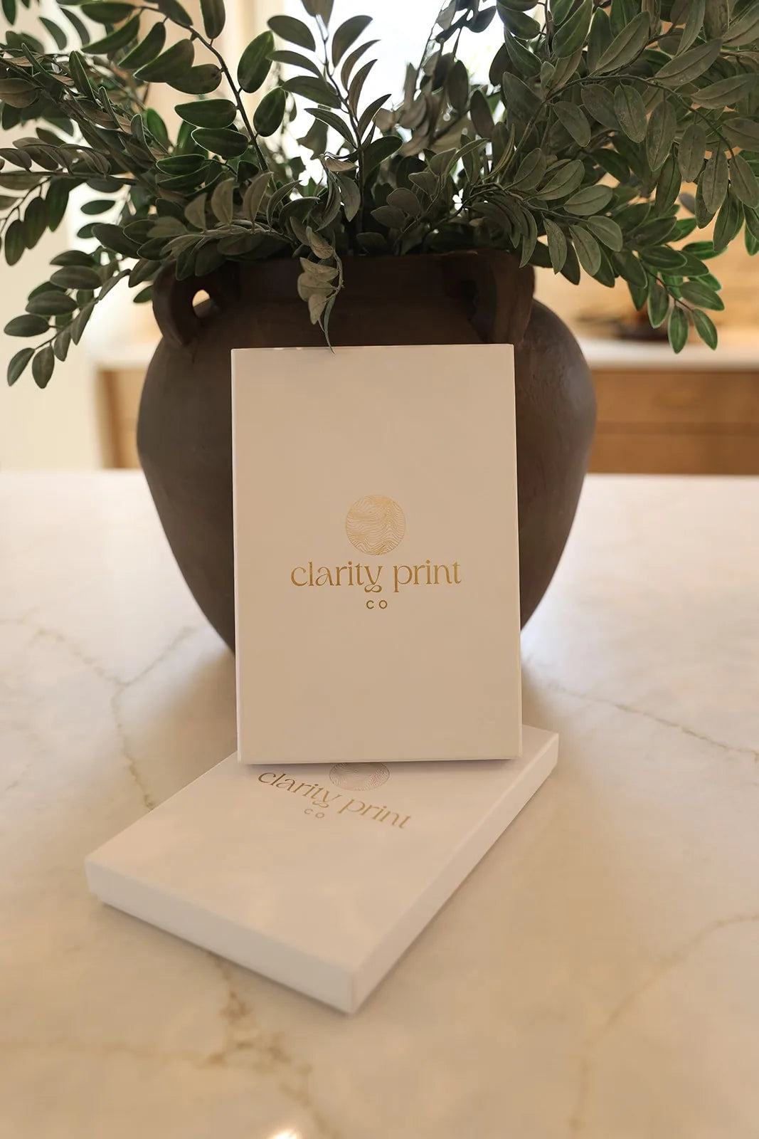 Vase with greenery and a card displaying 'clarity print' on a marble surface